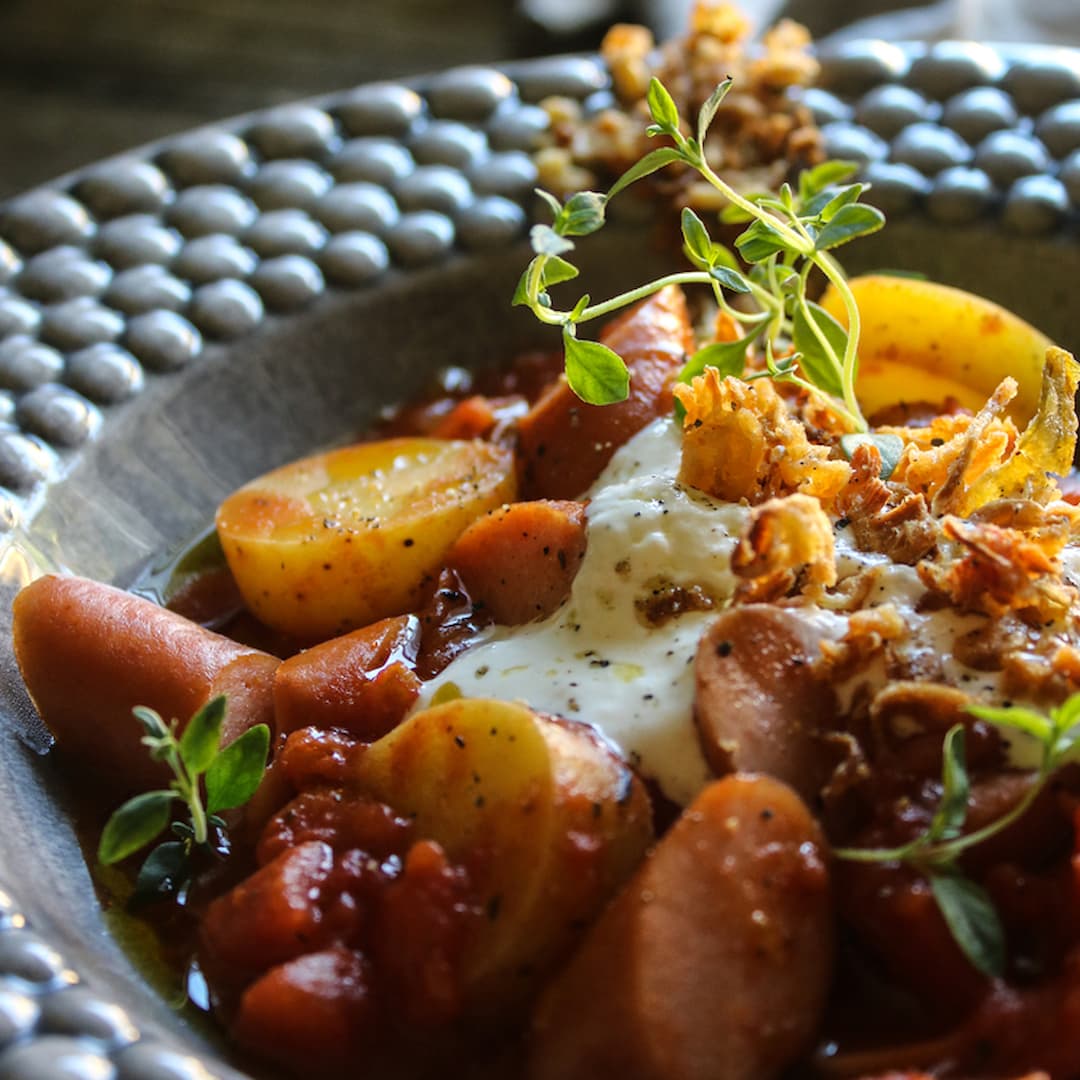 Örtig tomatgryta med wienerkorv toppas med parmesankräm och rostad lök